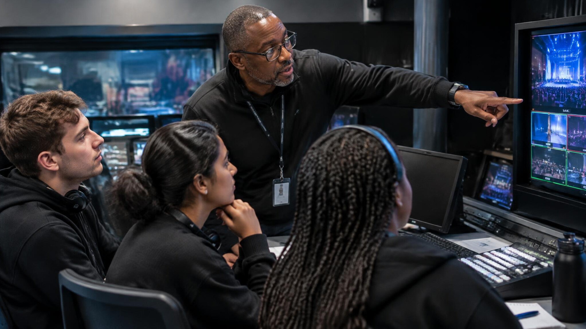 Trainer coaching a small crew around a monitor in a production gallery